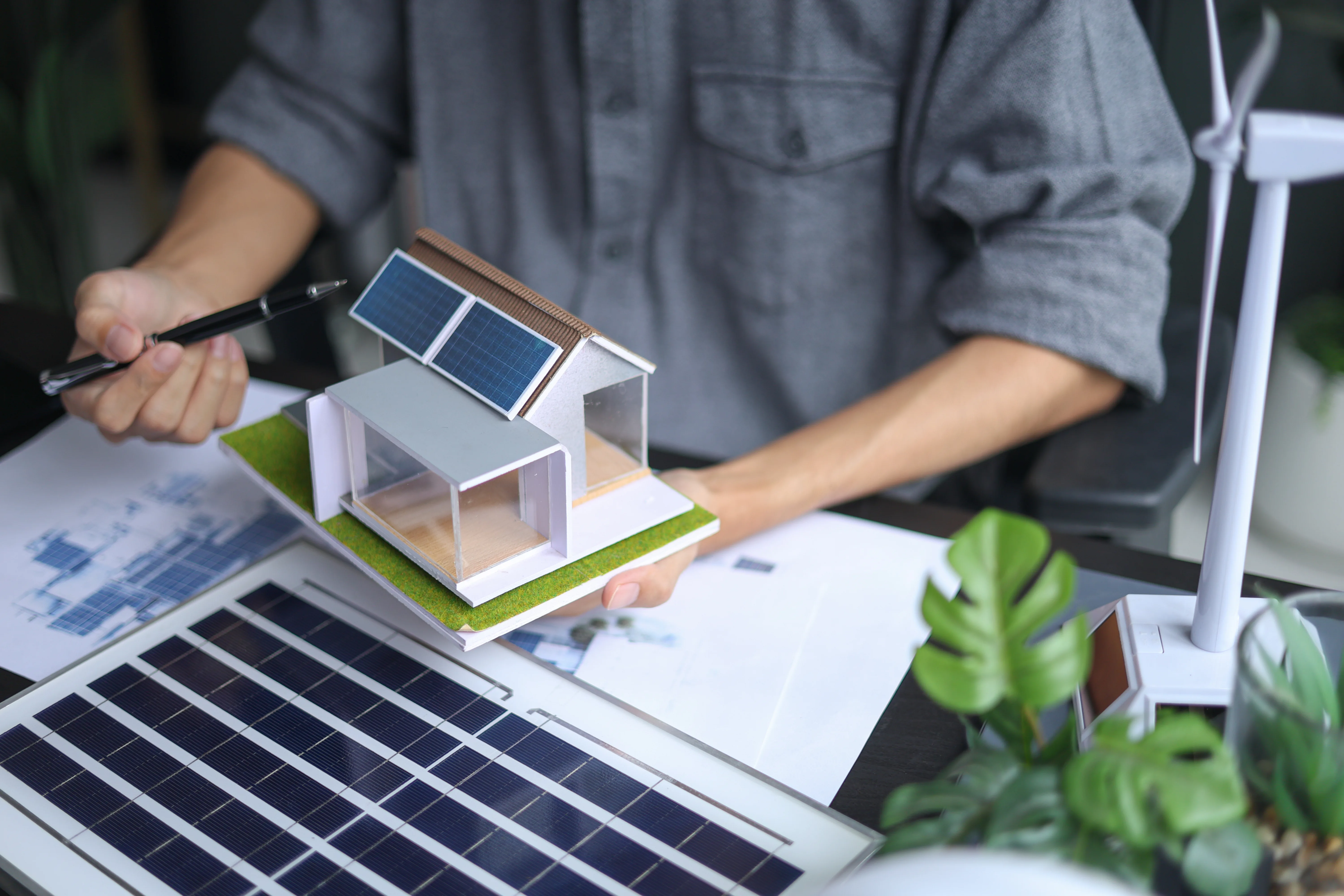 CoopGeeni y proyectos de vivienda sostenible con energía renovable Profesional trabajando con una maqueta de vivienda sostenible equipada con paneles solares y soluciones de energía renovable